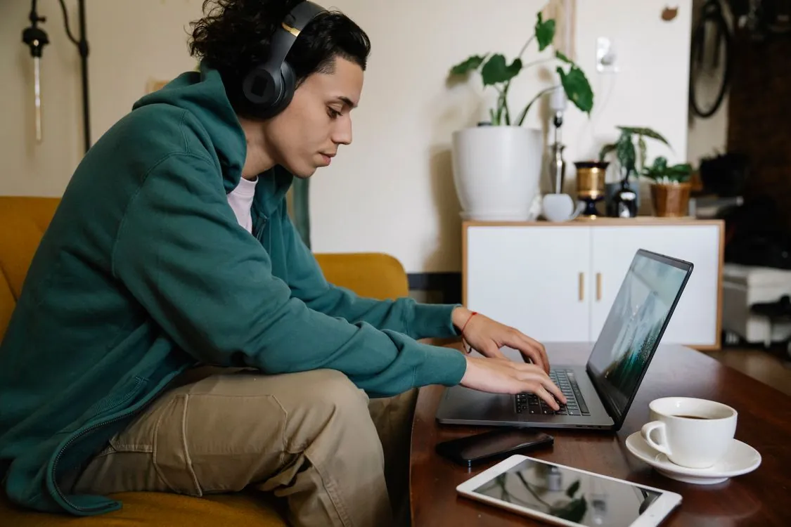 remote jobs no experience no degree - young man working from home on laptop with headphones and coffee